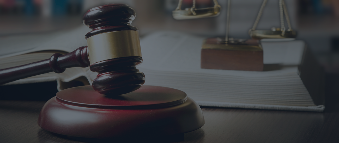 A wooden gavel with an open book and scales of justice in the background on a desk